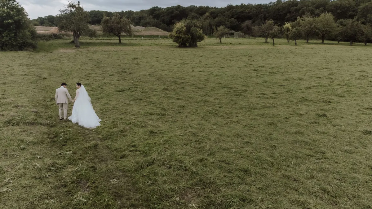 Video aéreo de boda: novios caminando por un campo abierto vistos desde un dron