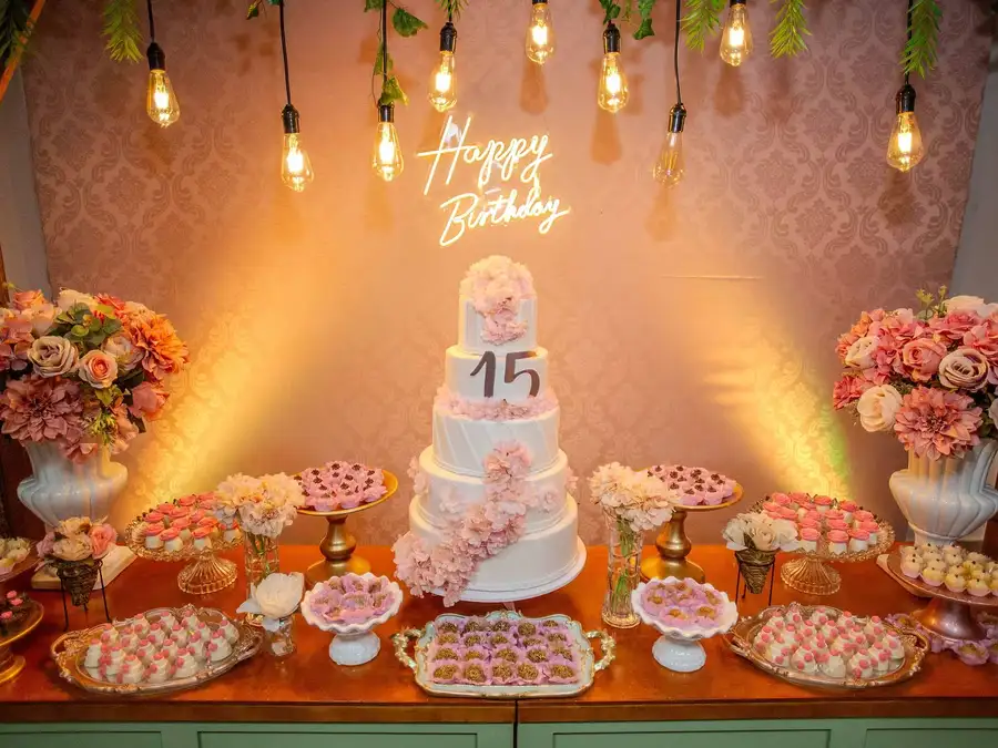 Mesa de dulces para XV años con pastel, flores y decoración rosa